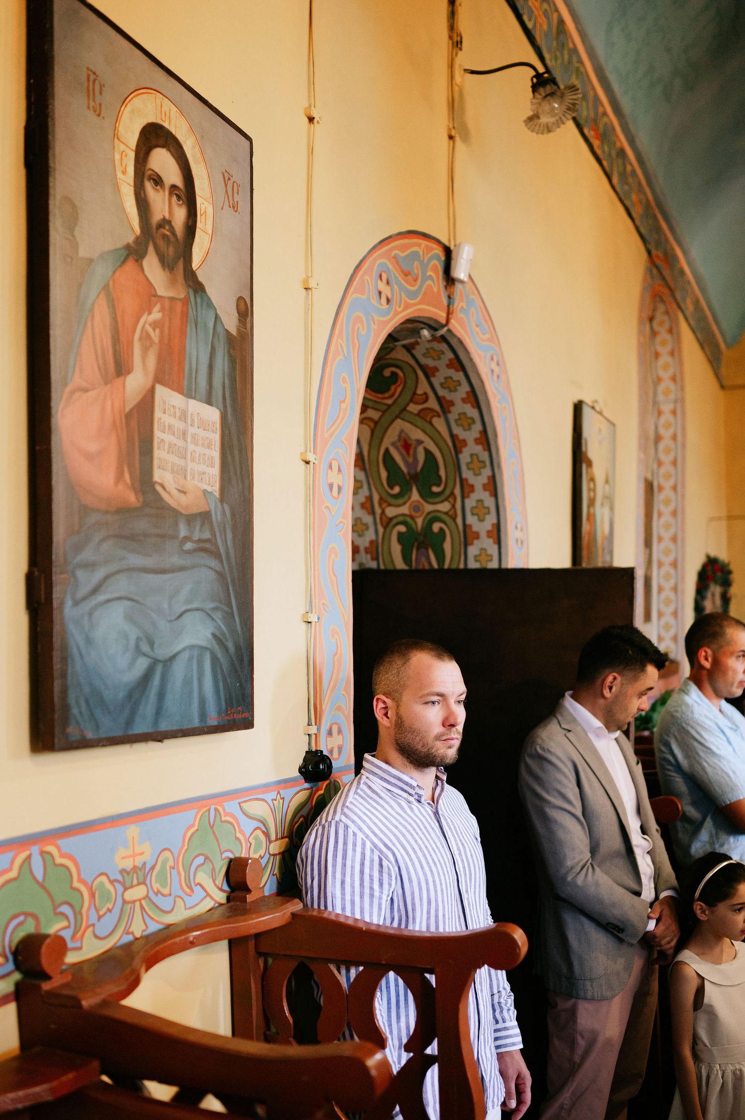 Religious murals and icons adorn the walls of a traditional Orthodox church during a ceremony.