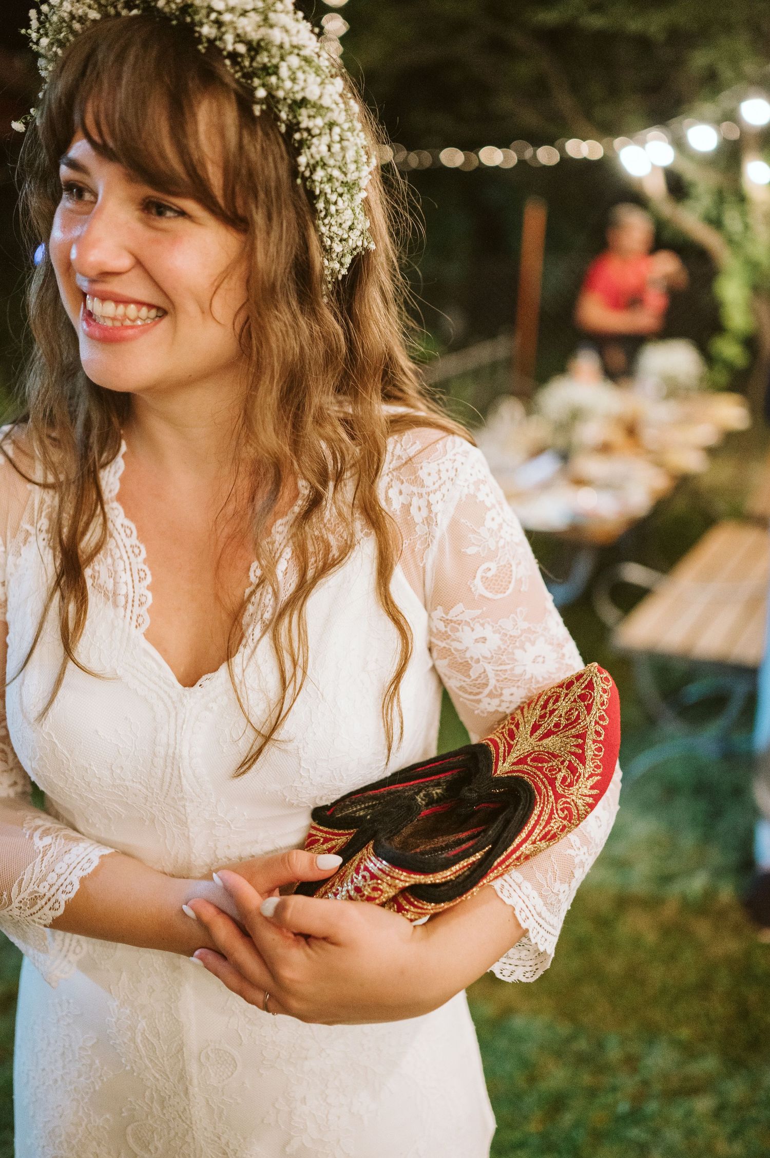Bride in lace dress holding a rooster during rustic outdoor wedding celebration.