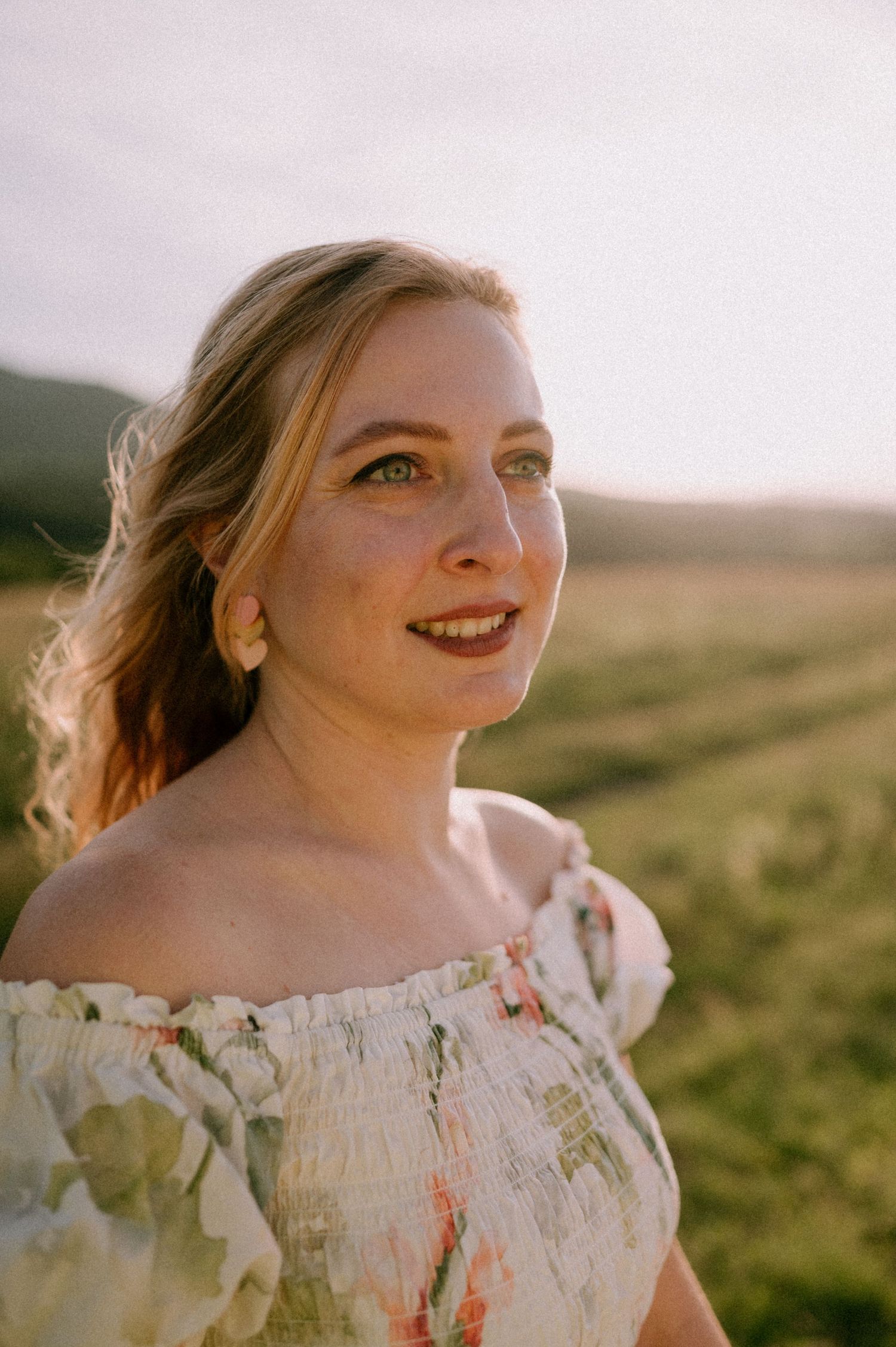 Portrait of a woman in floral dress against a sunset landscape.