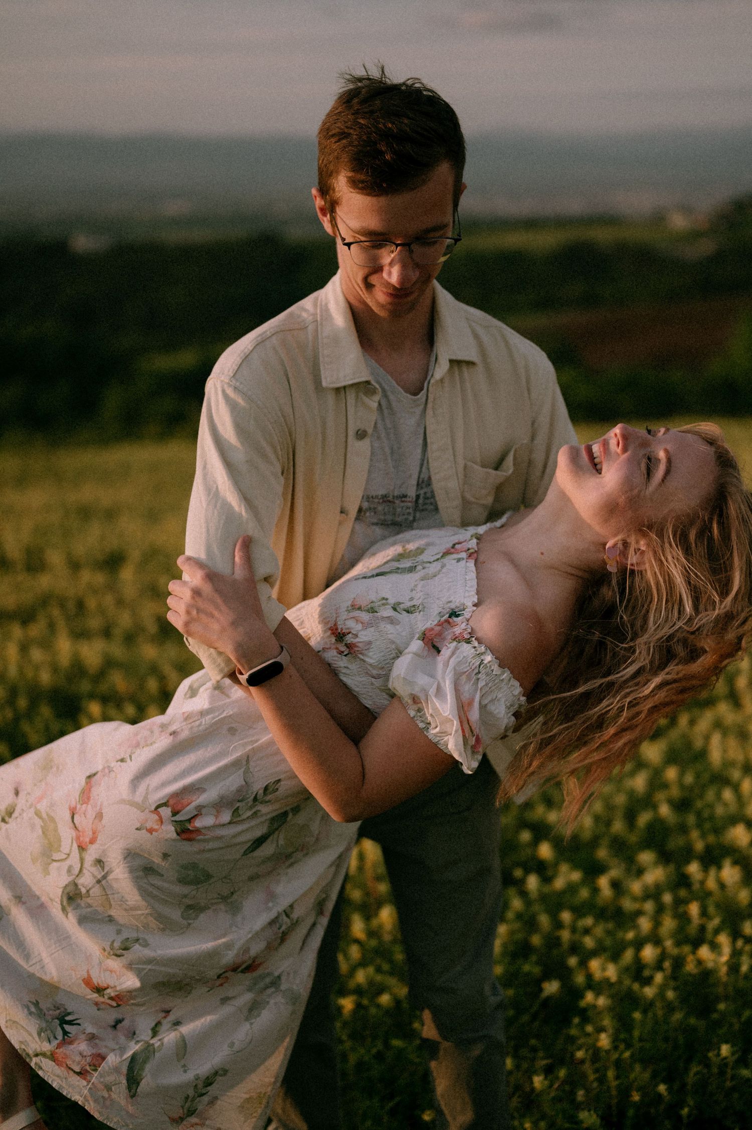 A romantic couple embraces in a field of yellow flowers during golden hour.