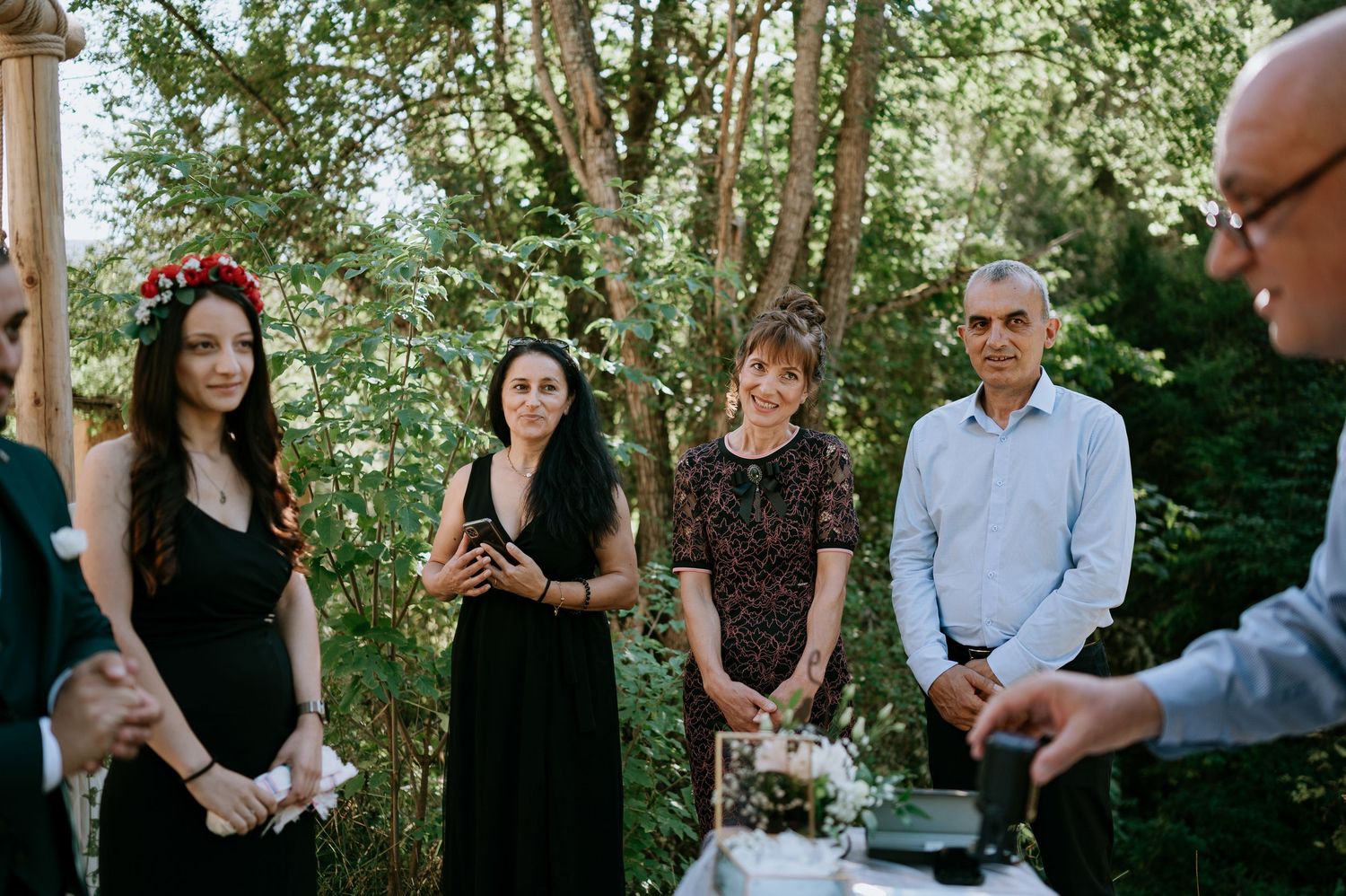Wedding guests mingle in a scenic outdoor garden setting surrounded by trees.