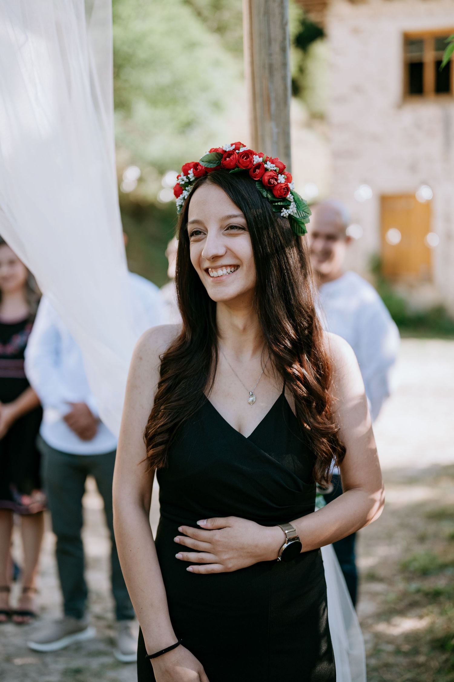 A person wearing a red flower crown and black dress smiles during an outdoor celebration.