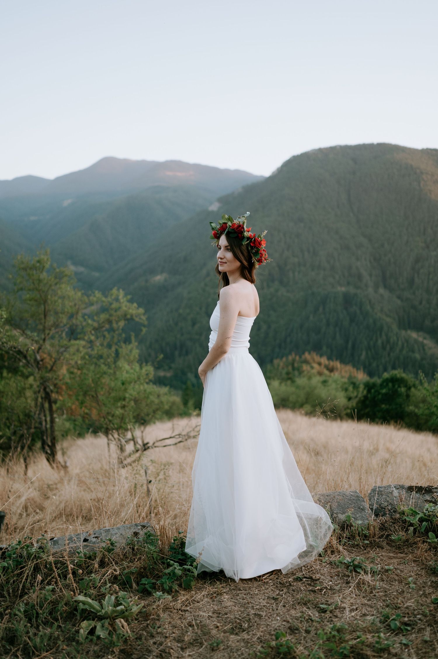 A flowing white wedding dress twirls against a mountainous landscape at sunset.