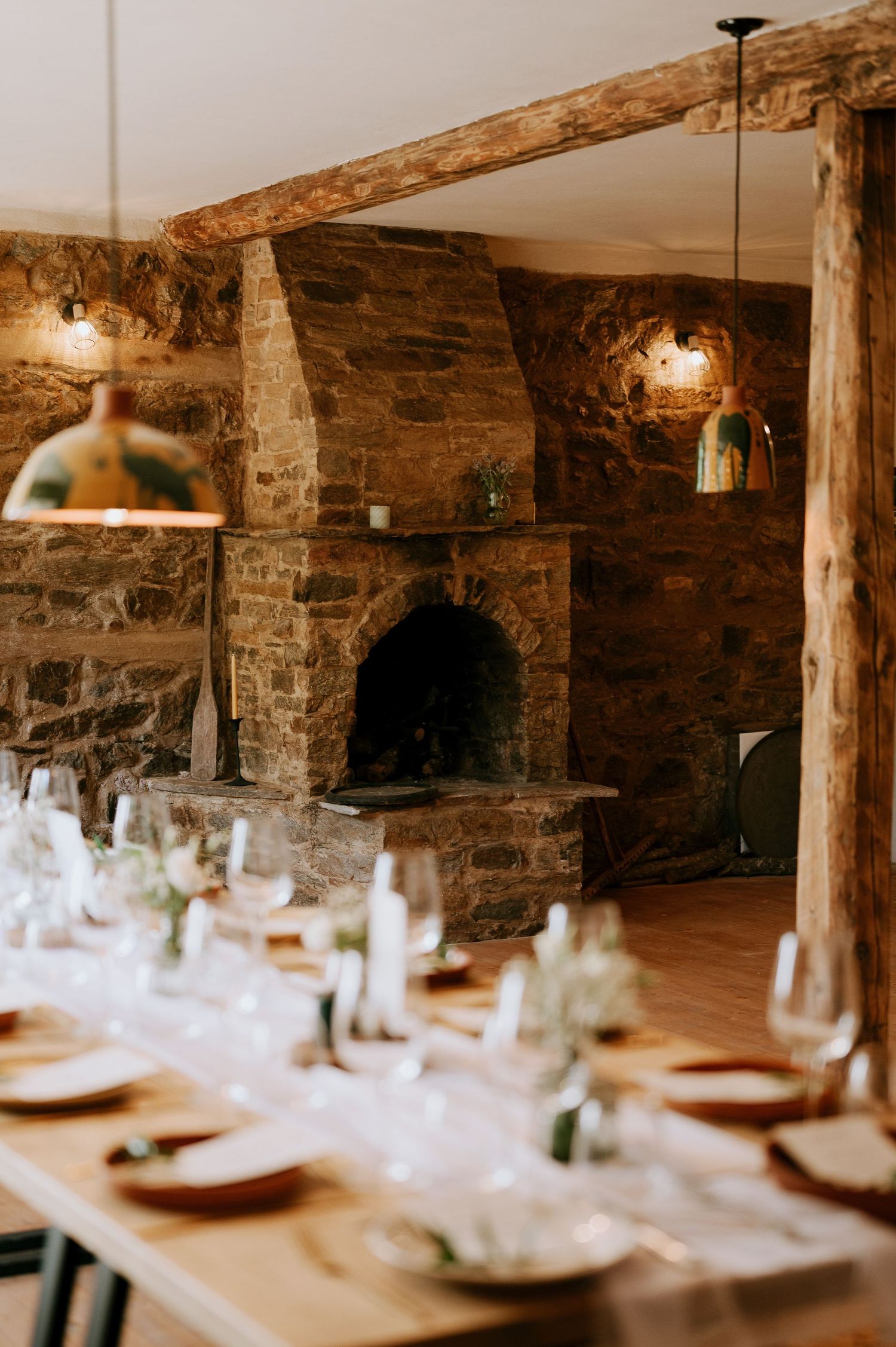Rustic stone dining room with wooden beams and long table set for elegant dinner service.