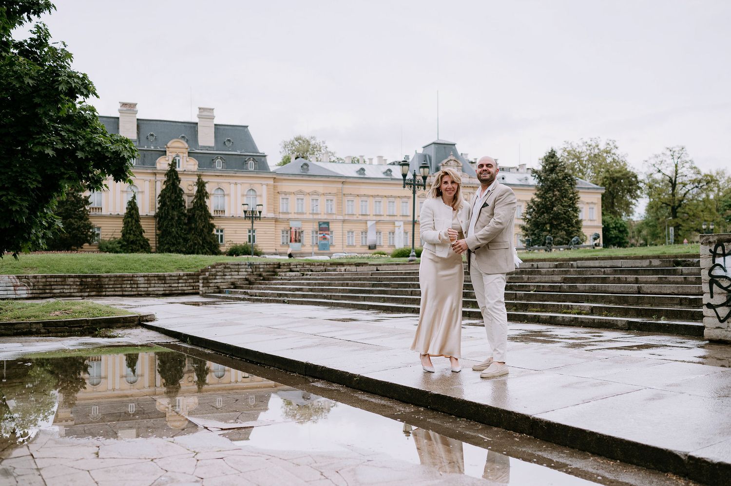 Elegant couple photographed against the backdrop of a historic palace and reflecting pool.