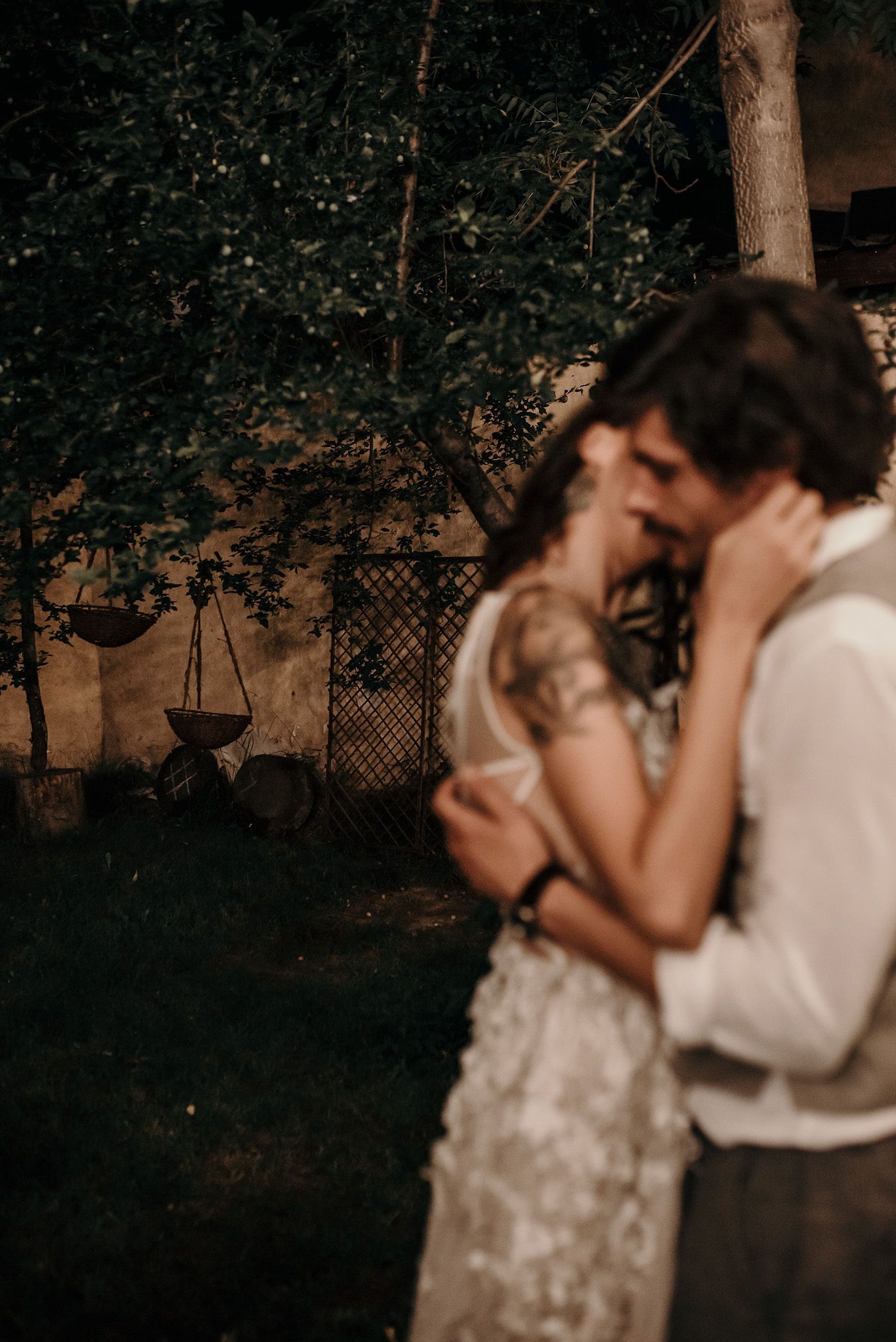 A romantic wedding couple shares an intimate dance together in a dimly lit garden setting.