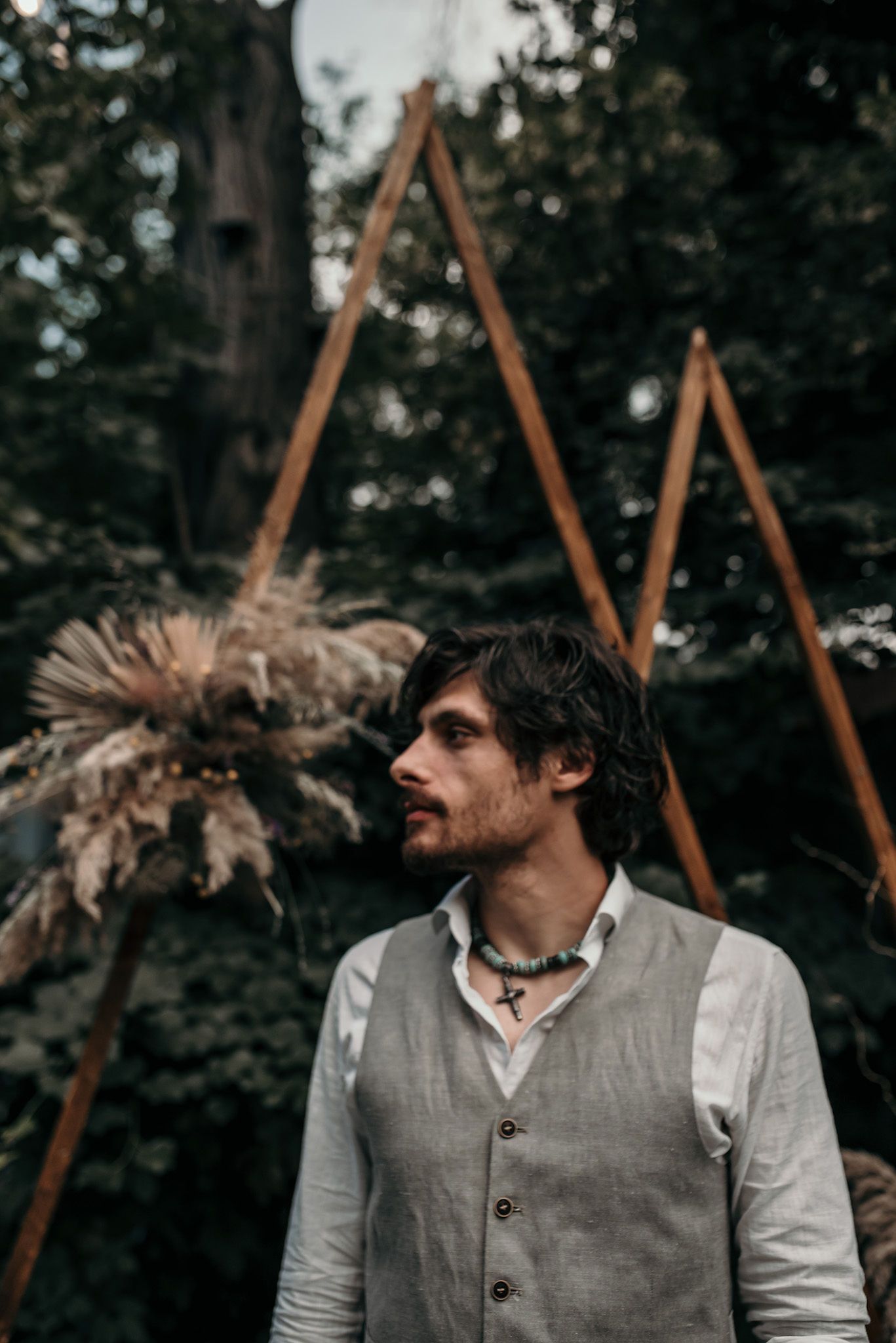 Artistic portrait in natural setting with wooden structures and dried pampas grass in background.