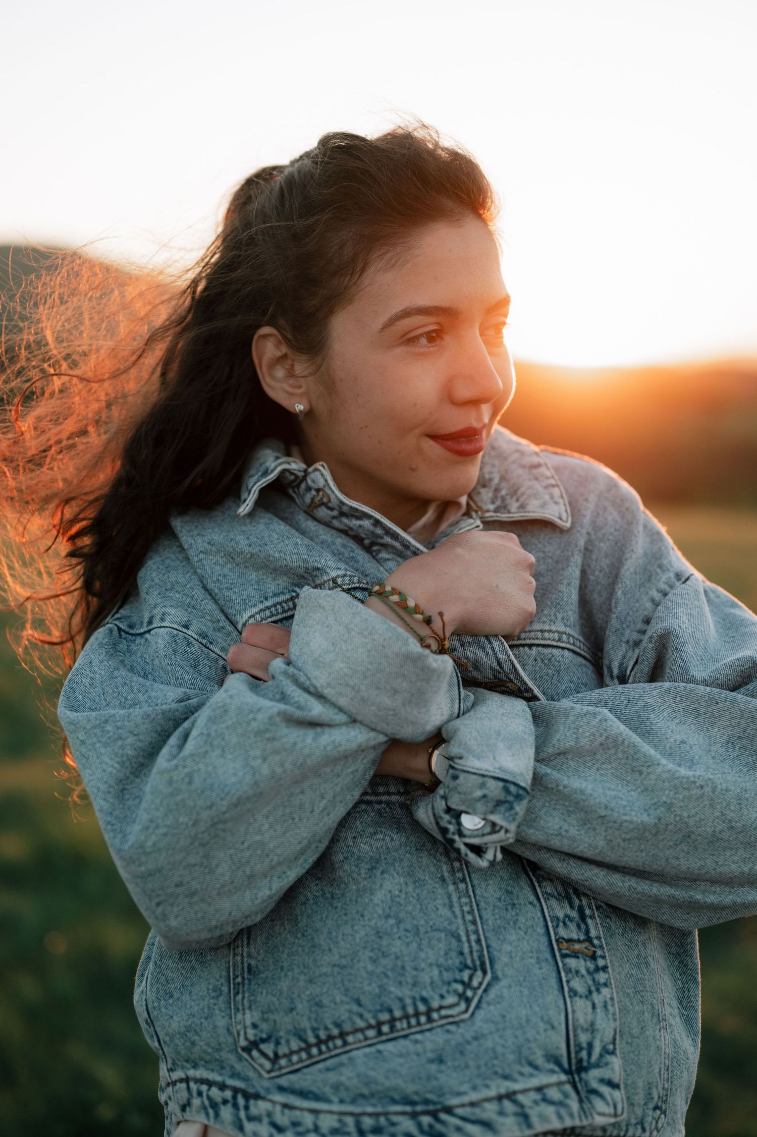Person wearing denim jacket smiles while posing against golden sunset light in artistic photo series.