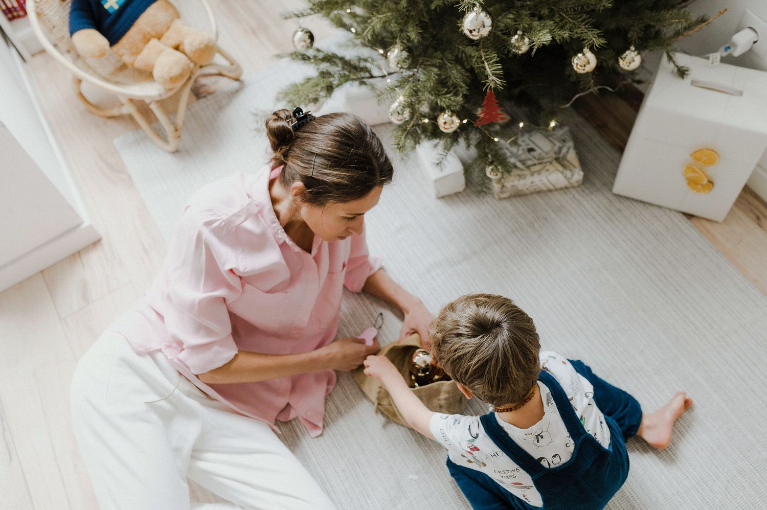 Two people sitting on floor next to Christmas tree wrapping presents together during holiday season.
