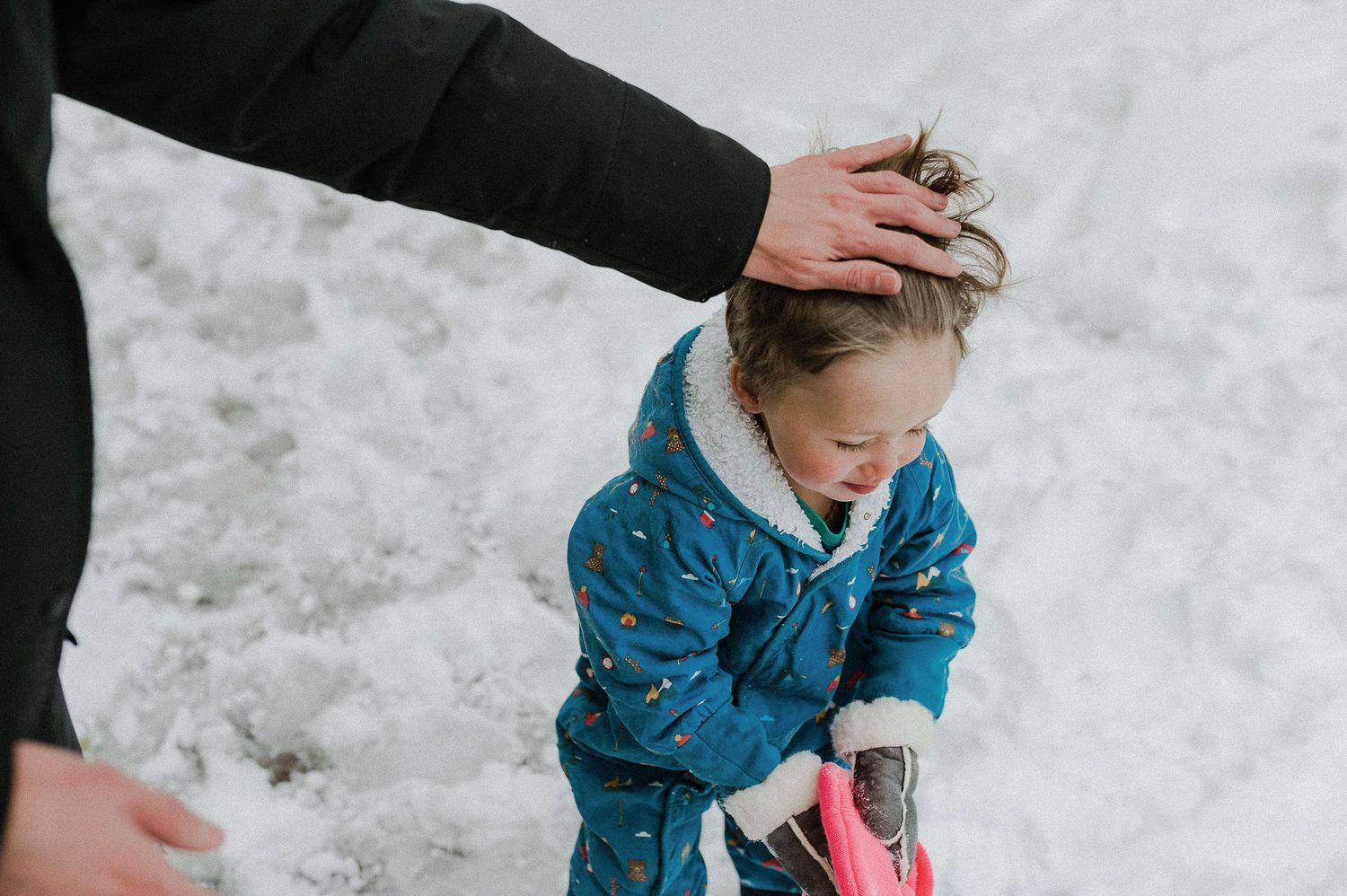 A person in a blue winter coat crouches down to play in the snow on a winter day.