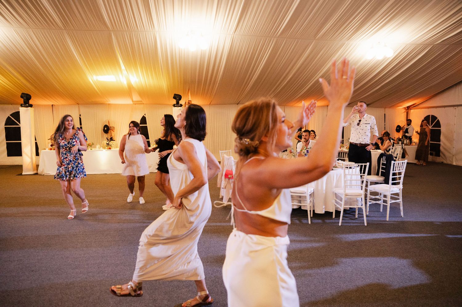 Wedding guests dancing and celebrating on the dance floor under warm lighting at an indoor reception venue.