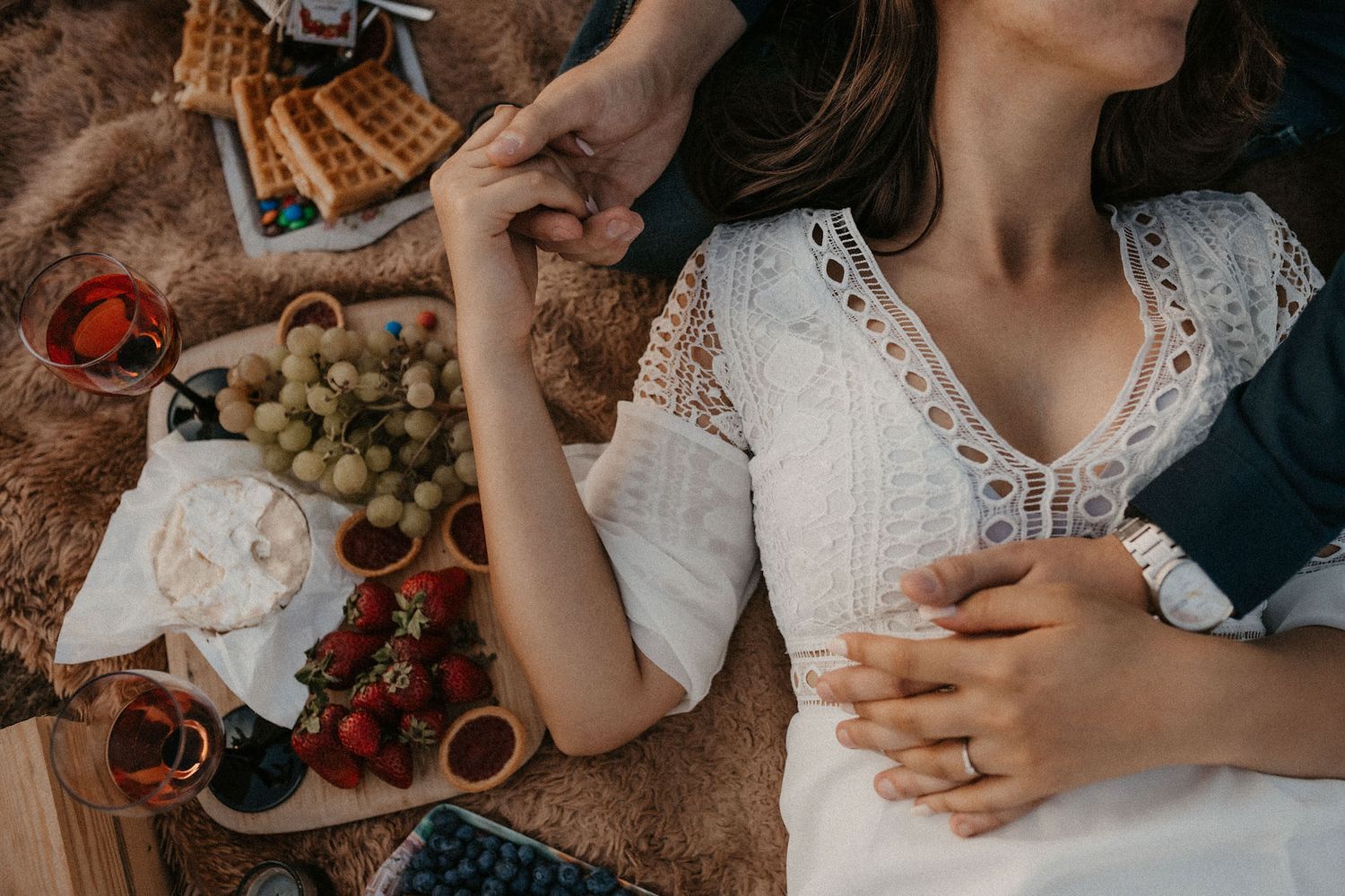 Romantic picnic scene with wine glasses and fresh fruit on textured blanket.