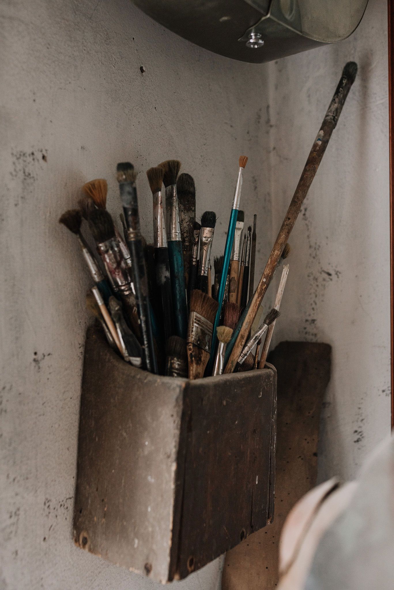 Collection of artist brushes and tools stored in rustic holders against a white wall.
