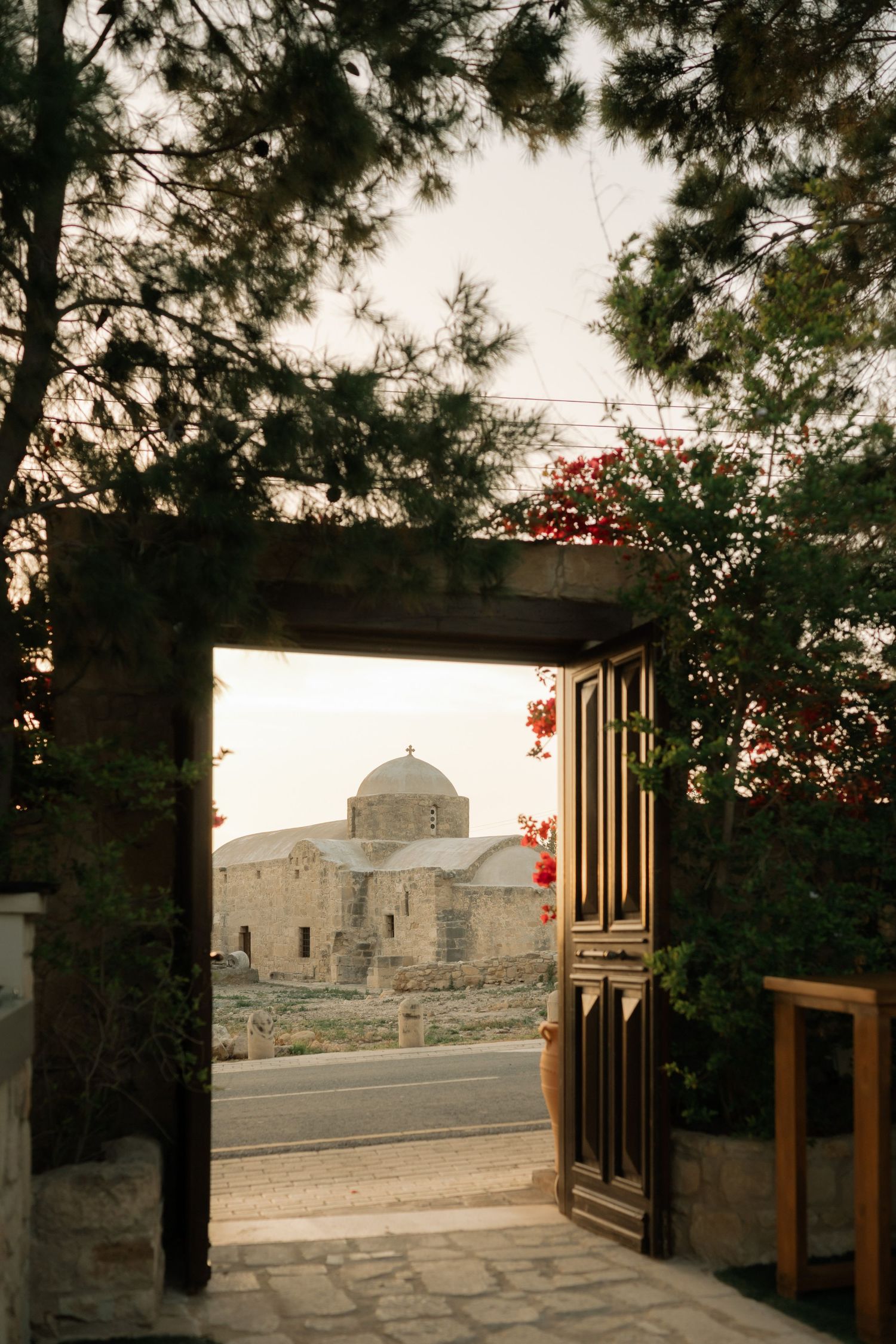 Ancient stone church with domed roof viewed through an open gate framed by trees at golden hour.