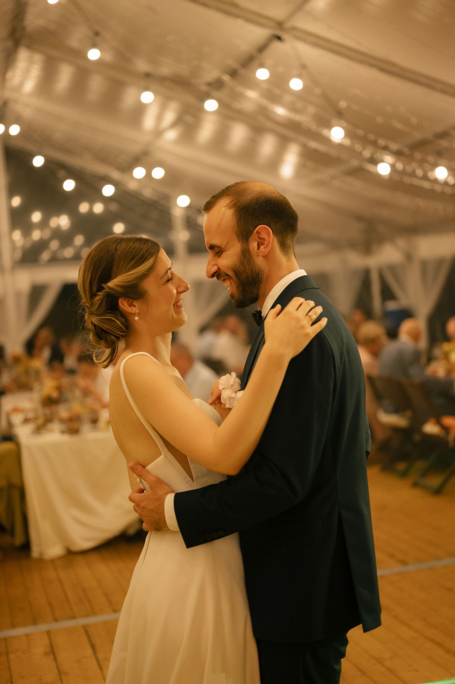 A couple shares their first dance at a wedding reception under twinkling lights in an elegant tent venue.