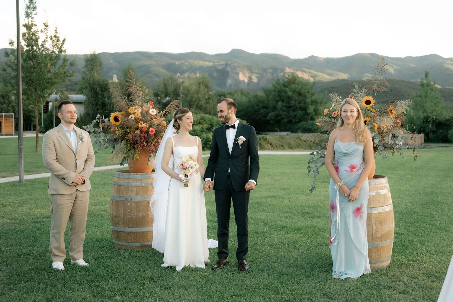 Wedding party members walk through a scenic vineyard with rolling hills and mountains in the background.
