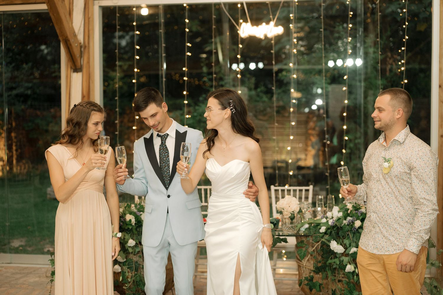 Wedding reception celebration with string lights and floral decor in a rustic indoor venue during evening festivities.