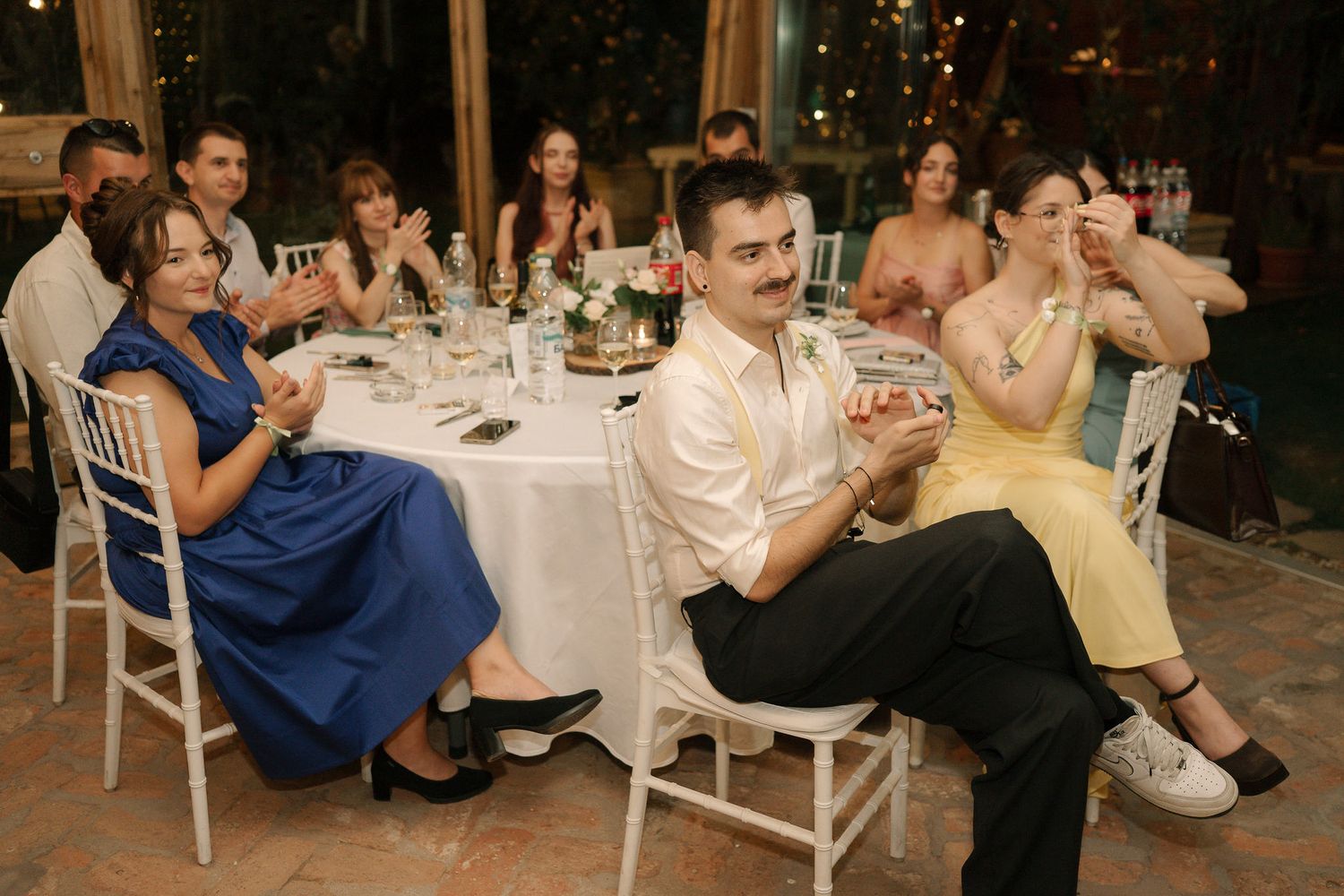 Wedding guests seated at reception tables share laughter and conversation during evening celebration.