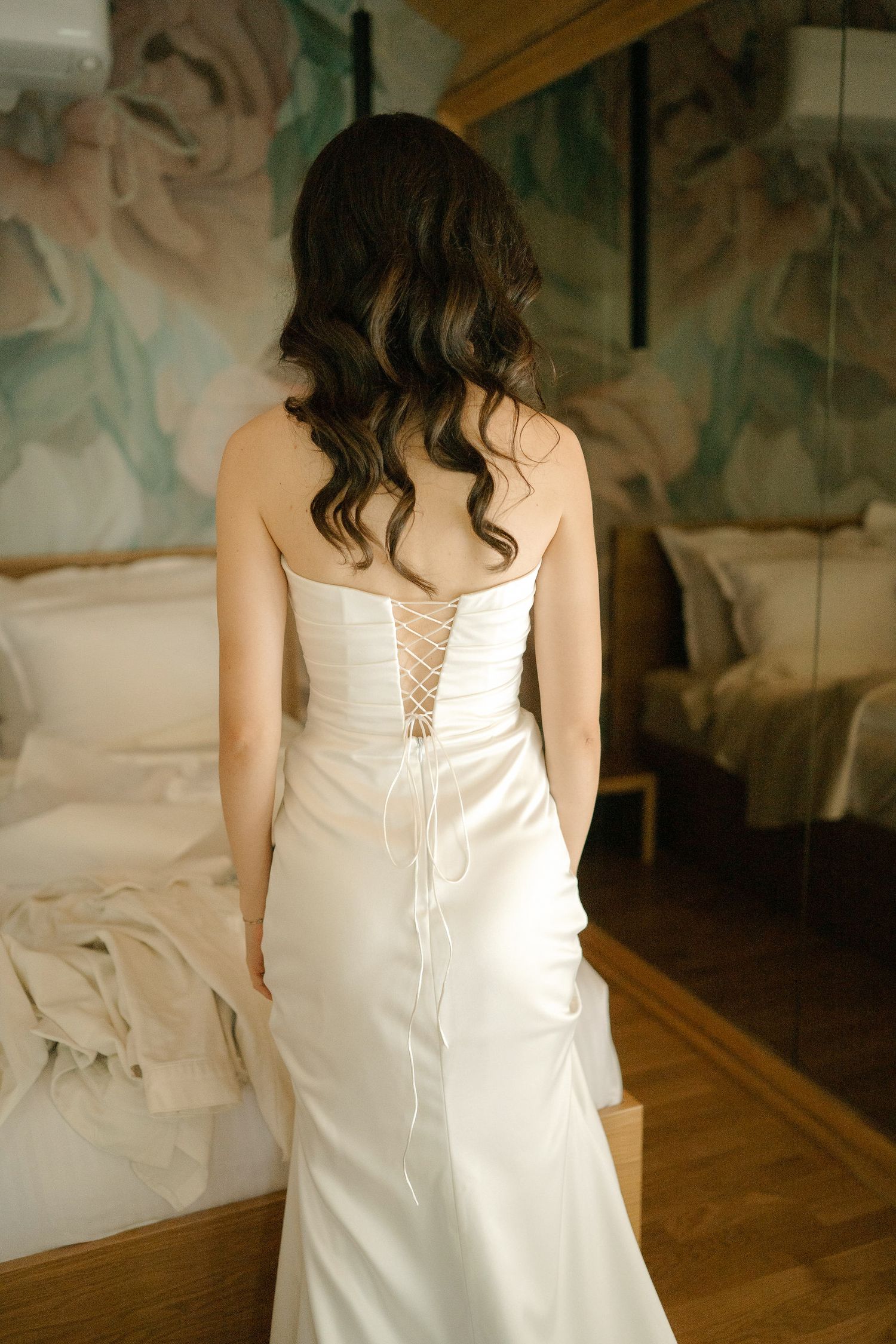 Back view of a white corset wedding dress with lace-up detail on a wooden floor.