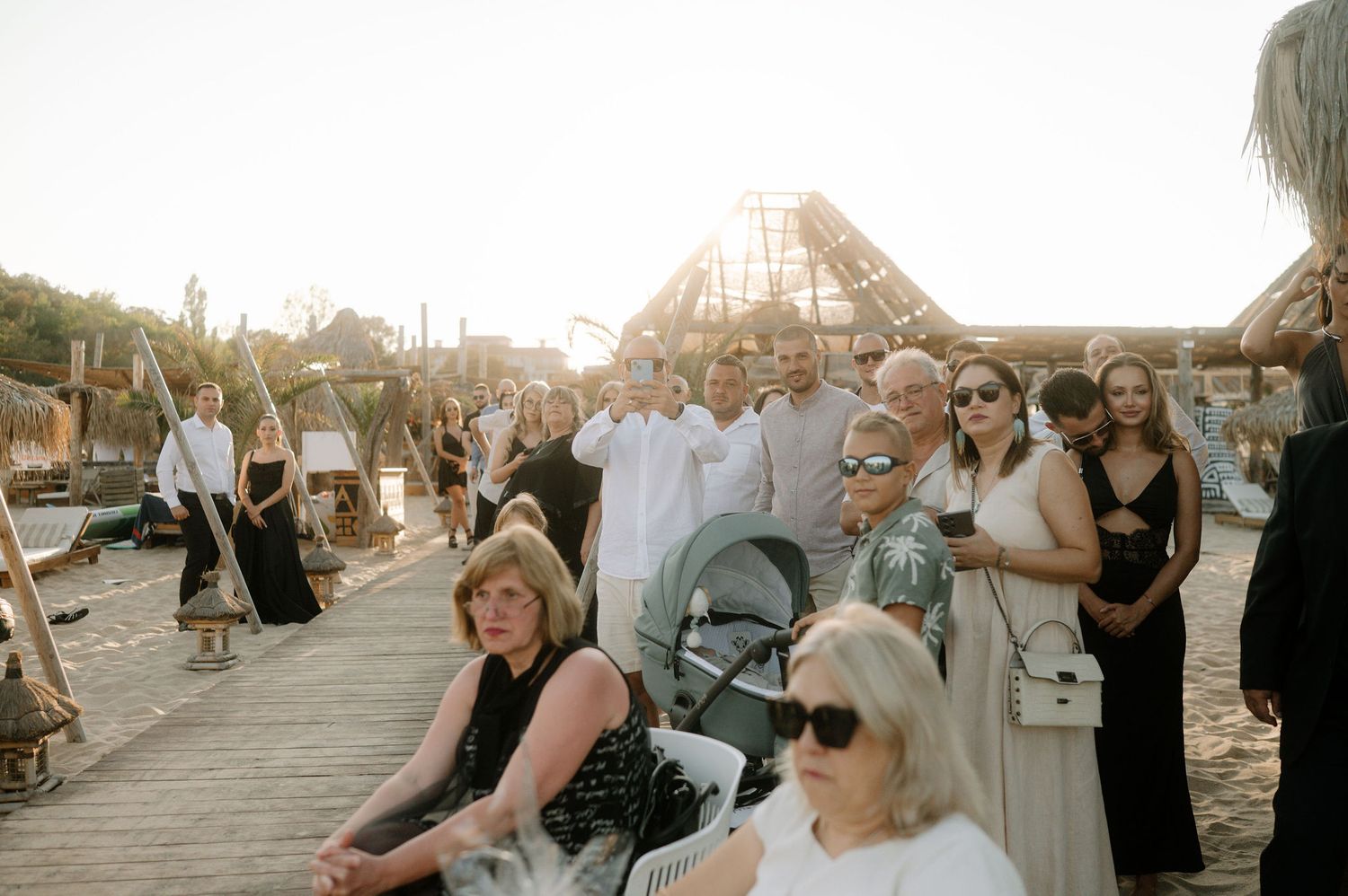 A series of candid moments at an outdoor wedding celebration with guests gathered on a wooden deck at sunset.