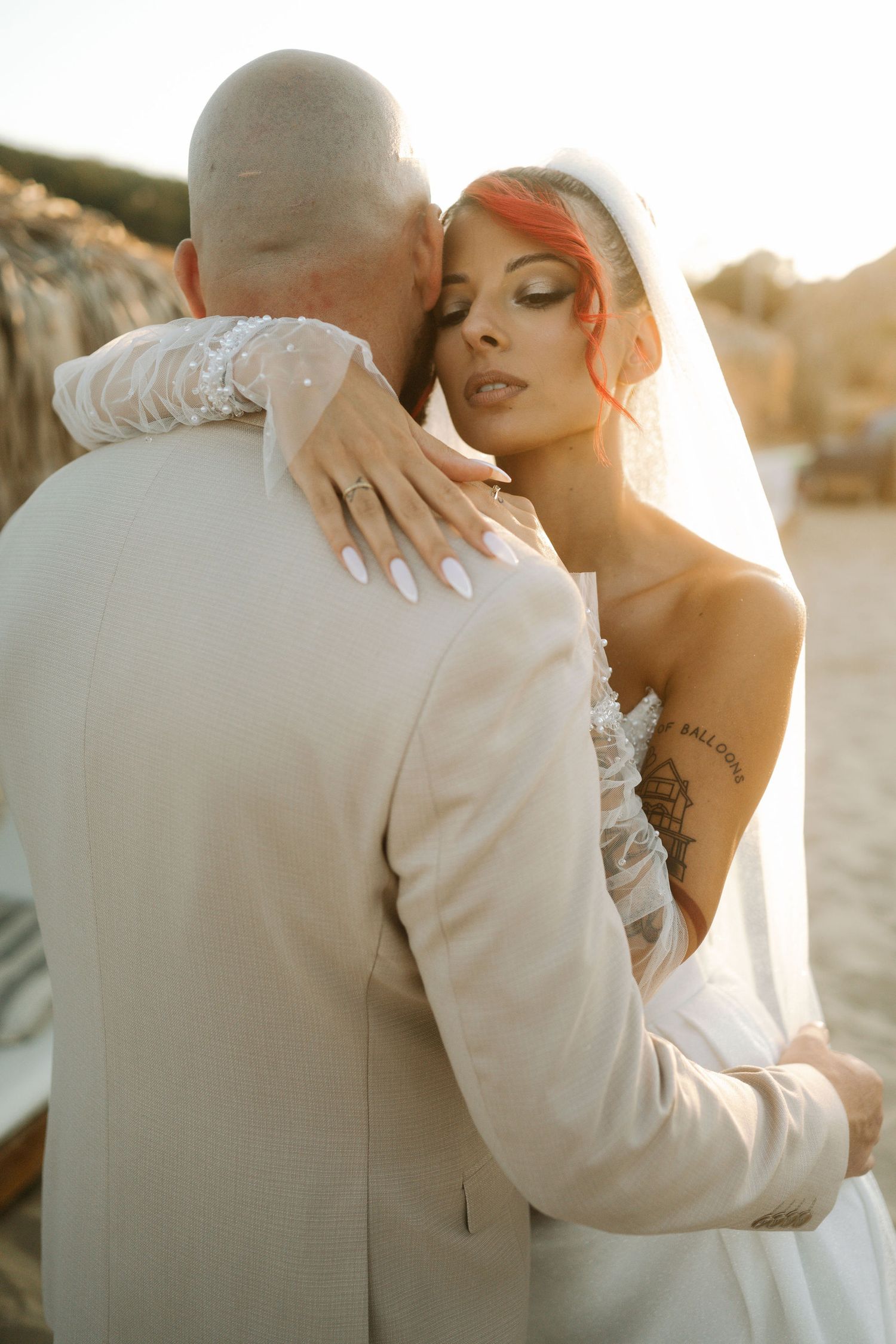 Romantic wedding couple embraces during golden hour sunset, with bride wearing white lace dress and delicate veil.