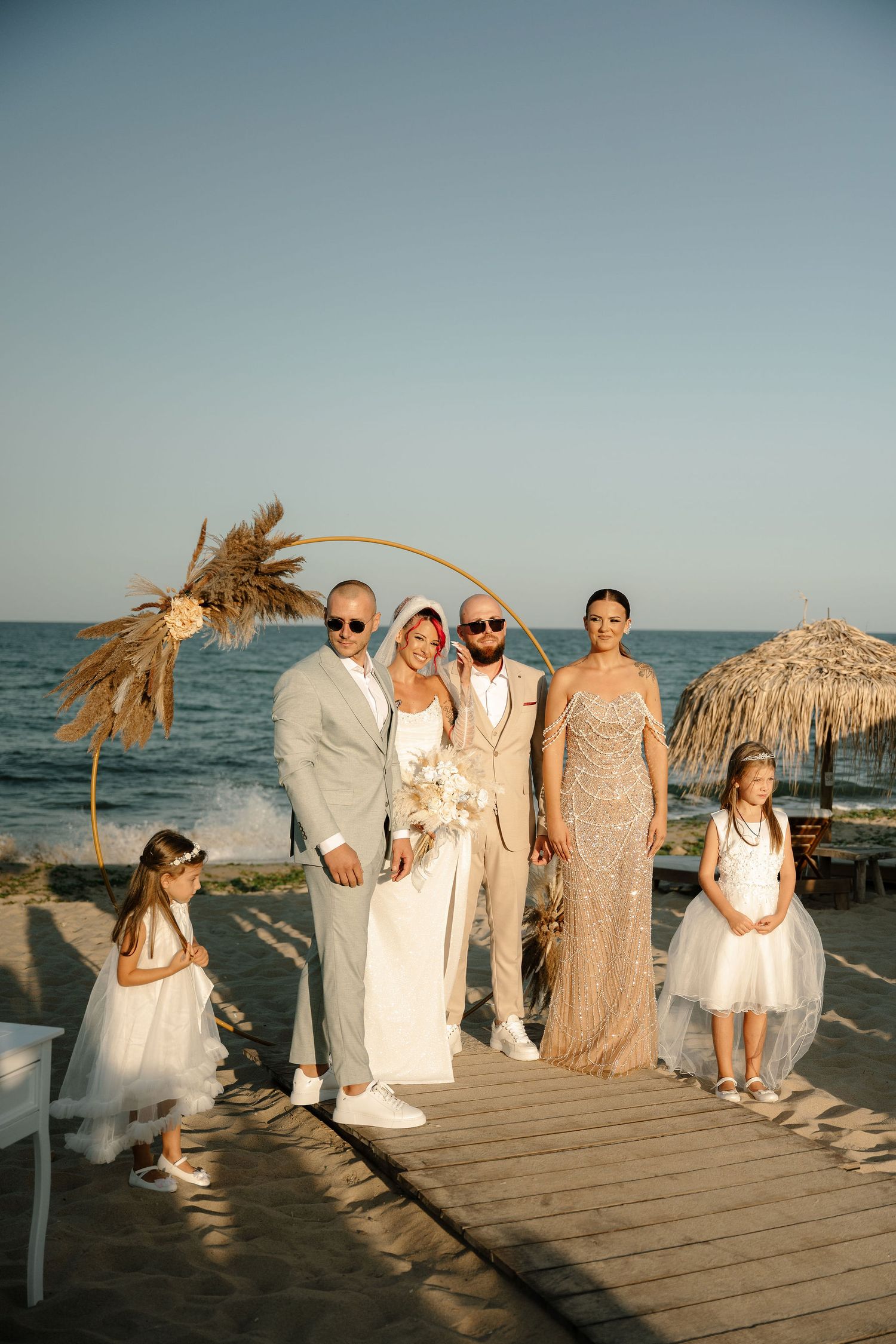 Wedding party poses together on a wooden dock at sunset with tiki umbrellas and ocean views in the background.