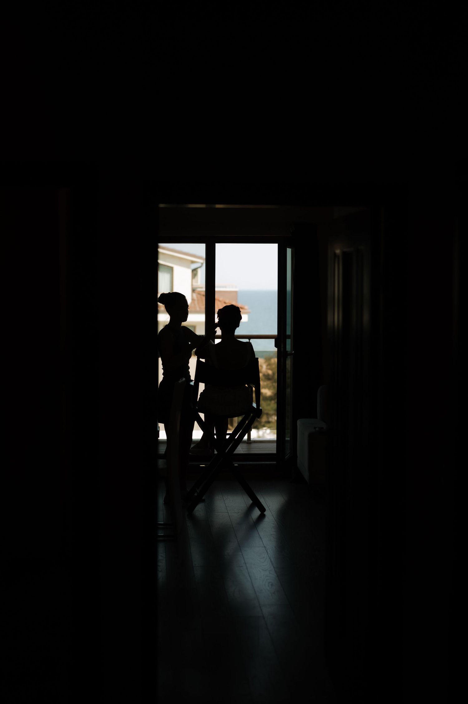 Silhouettes stand in a dark doorway framing an ocean view through a bright window.