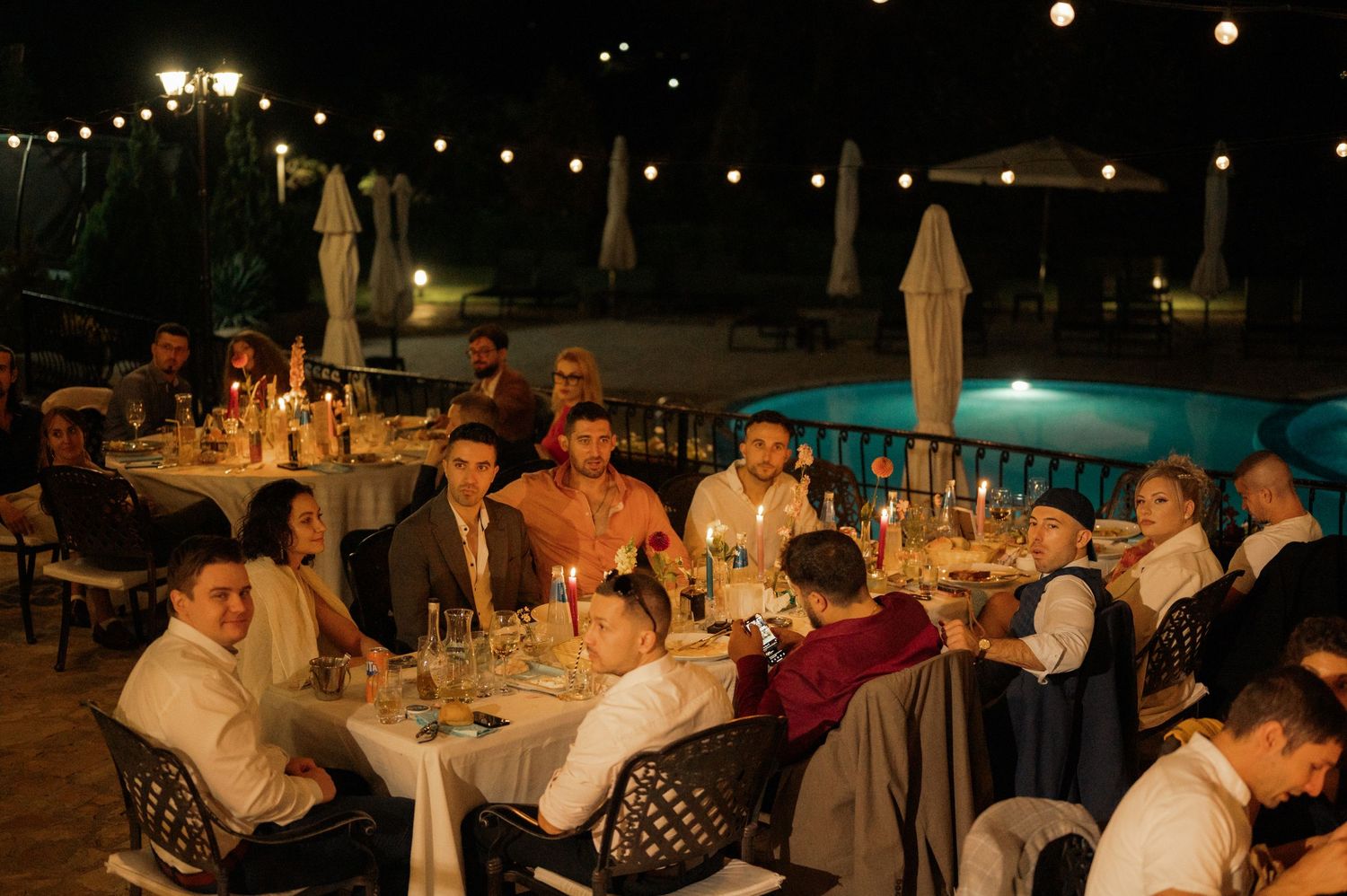 Diners enjoy an elegant evening meal at outdoor restaurant tables illuminated by warm lighting and string lights.