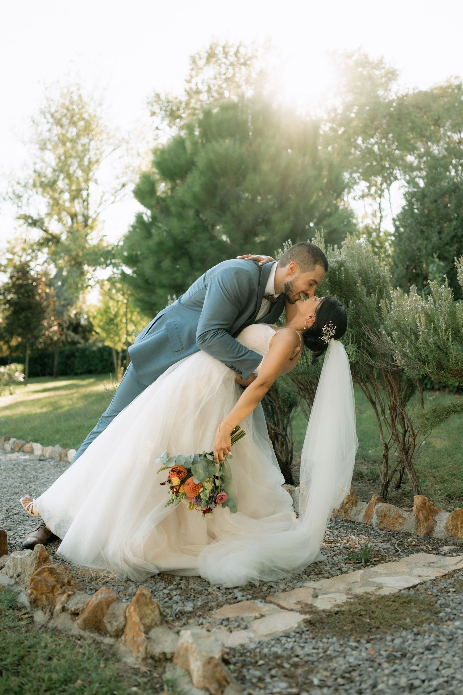 Romantic wedding couple shares tender moment on stone path with their golden retriever dog in sunset lighting.
