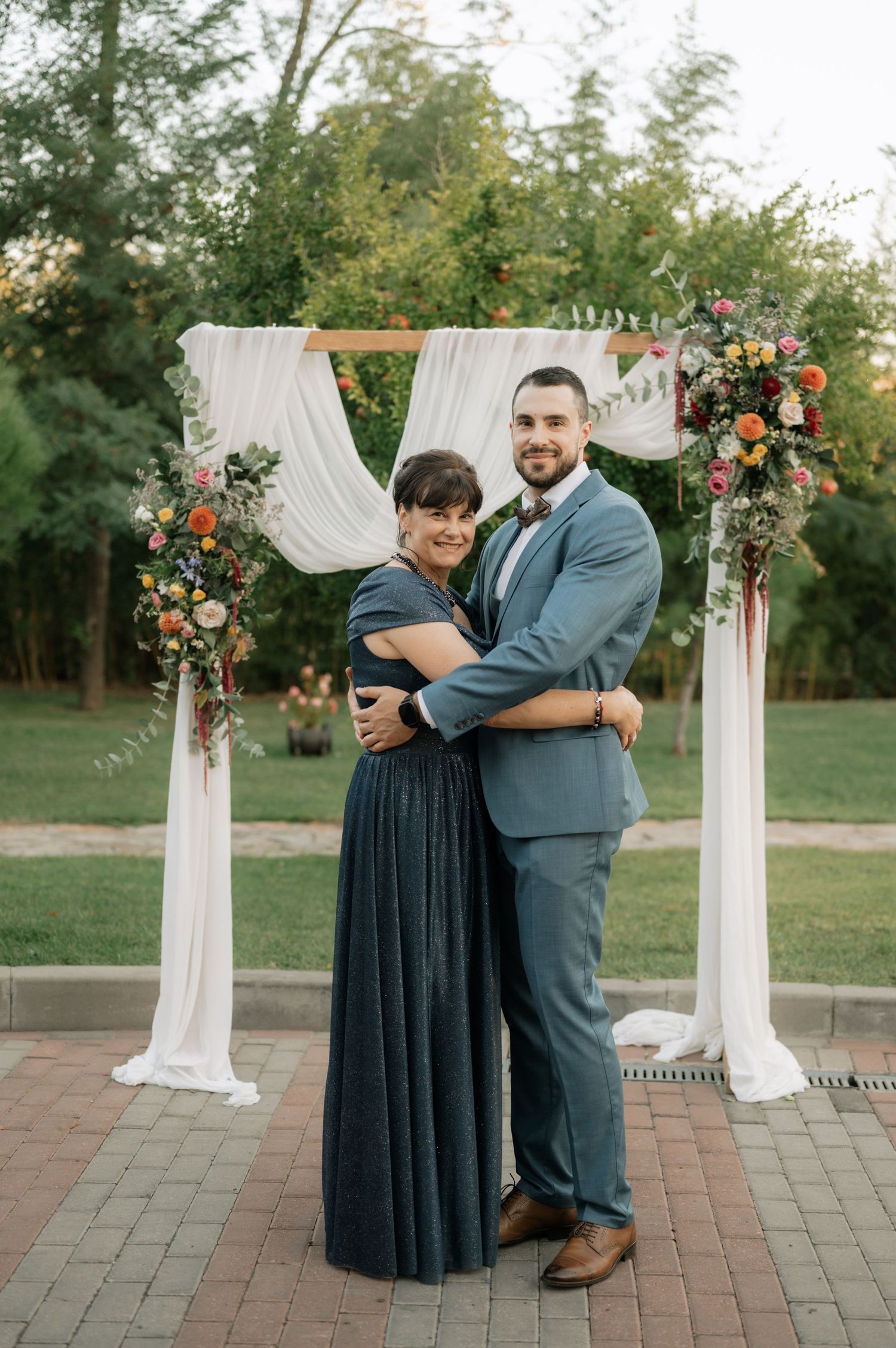 A couple shares an intimate moment under a floral wedding arch decorated with white fabric and pink flowers.