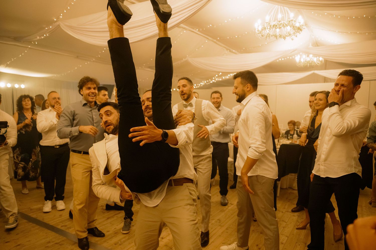 Man performing acrobatic handstand flip surrounded by cheering guests at an elegant wedding reception.