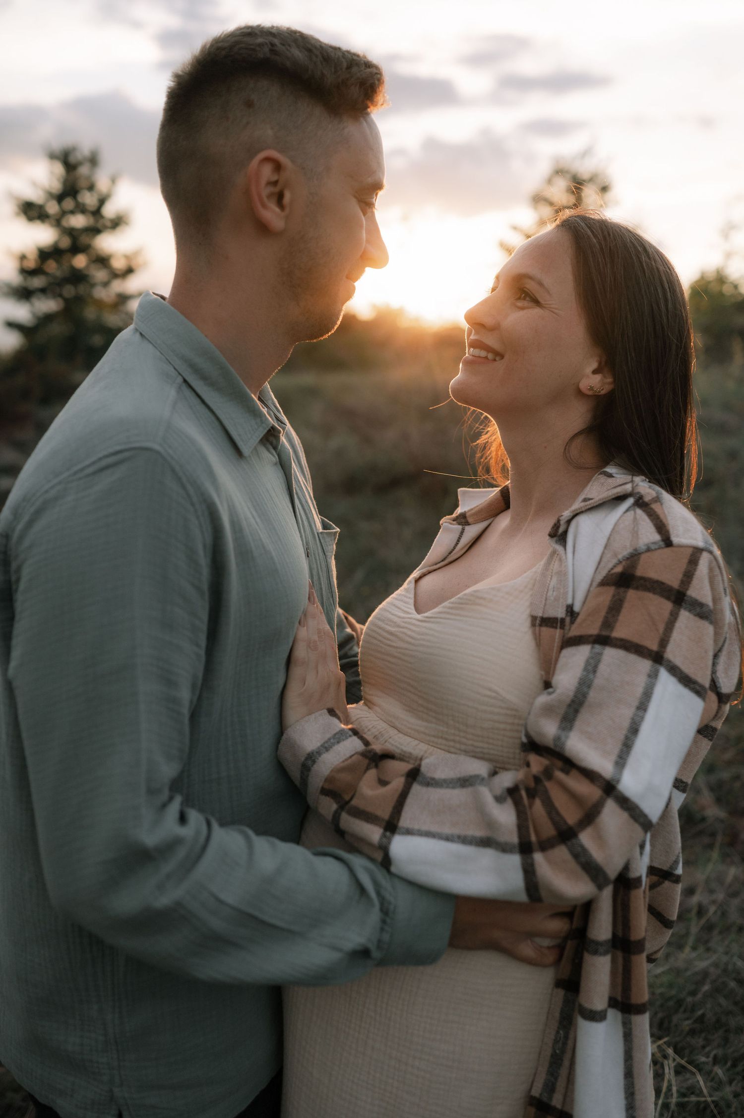 A couple shares intimate moments during a sunset photoshoot while wrapped in a cozy plaid blanket.