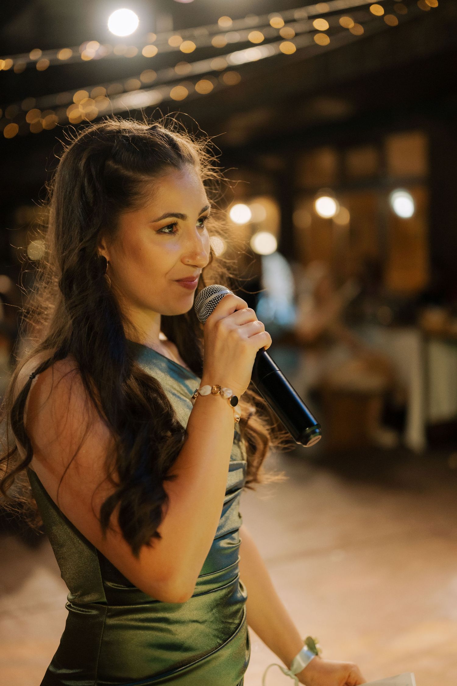 A woman in a green dress sits at a bar counter in dim lighting with bokeh effects in the background.
