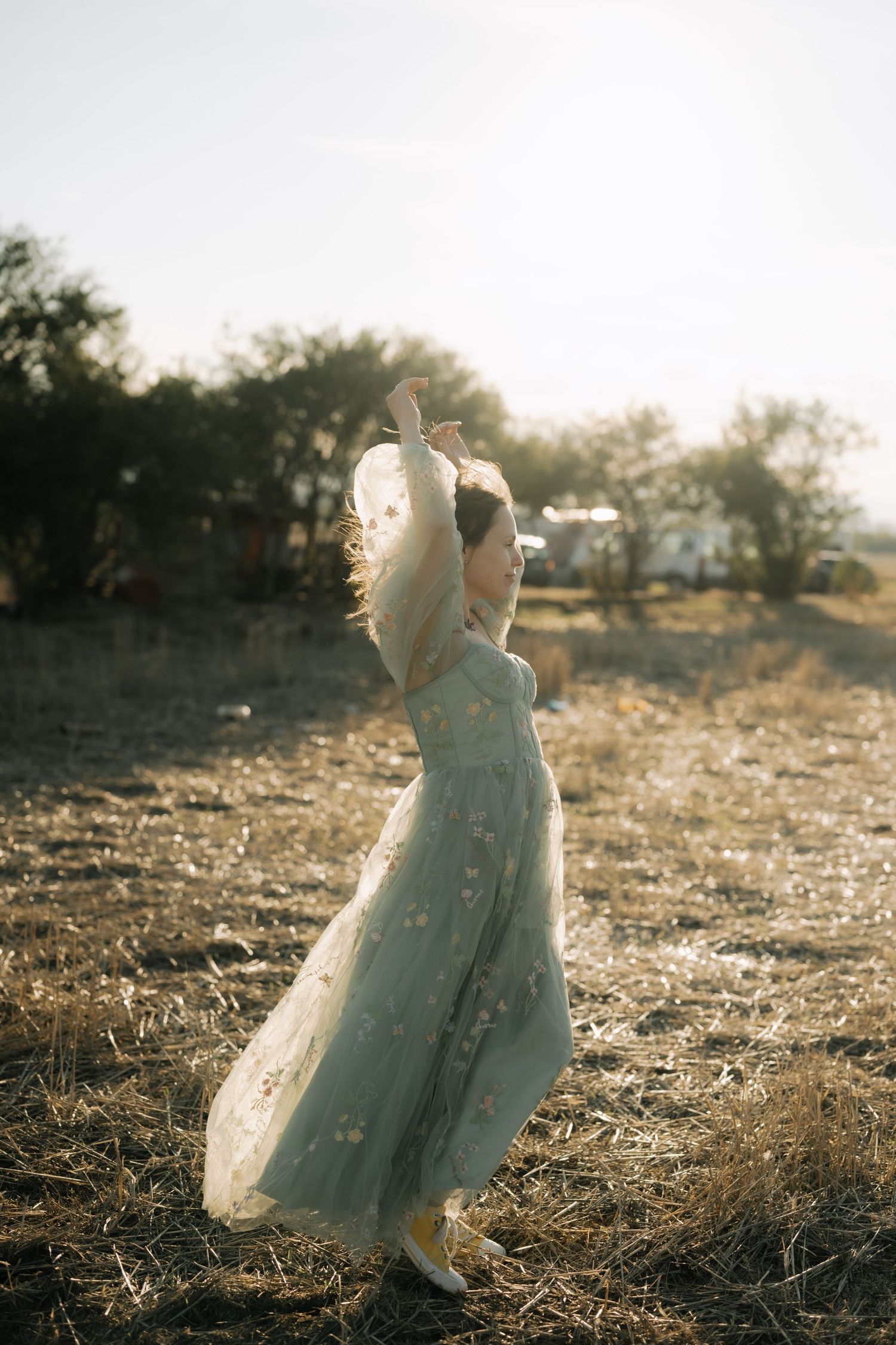 A child in a light blue vintage dress stands in a sunlit field during golden hour.