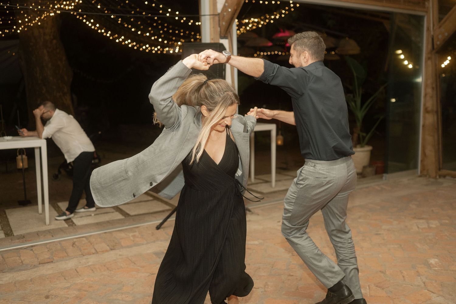 A couple performs a romantic dance dip sequence under twinkling string lights at an outdoor evening event.