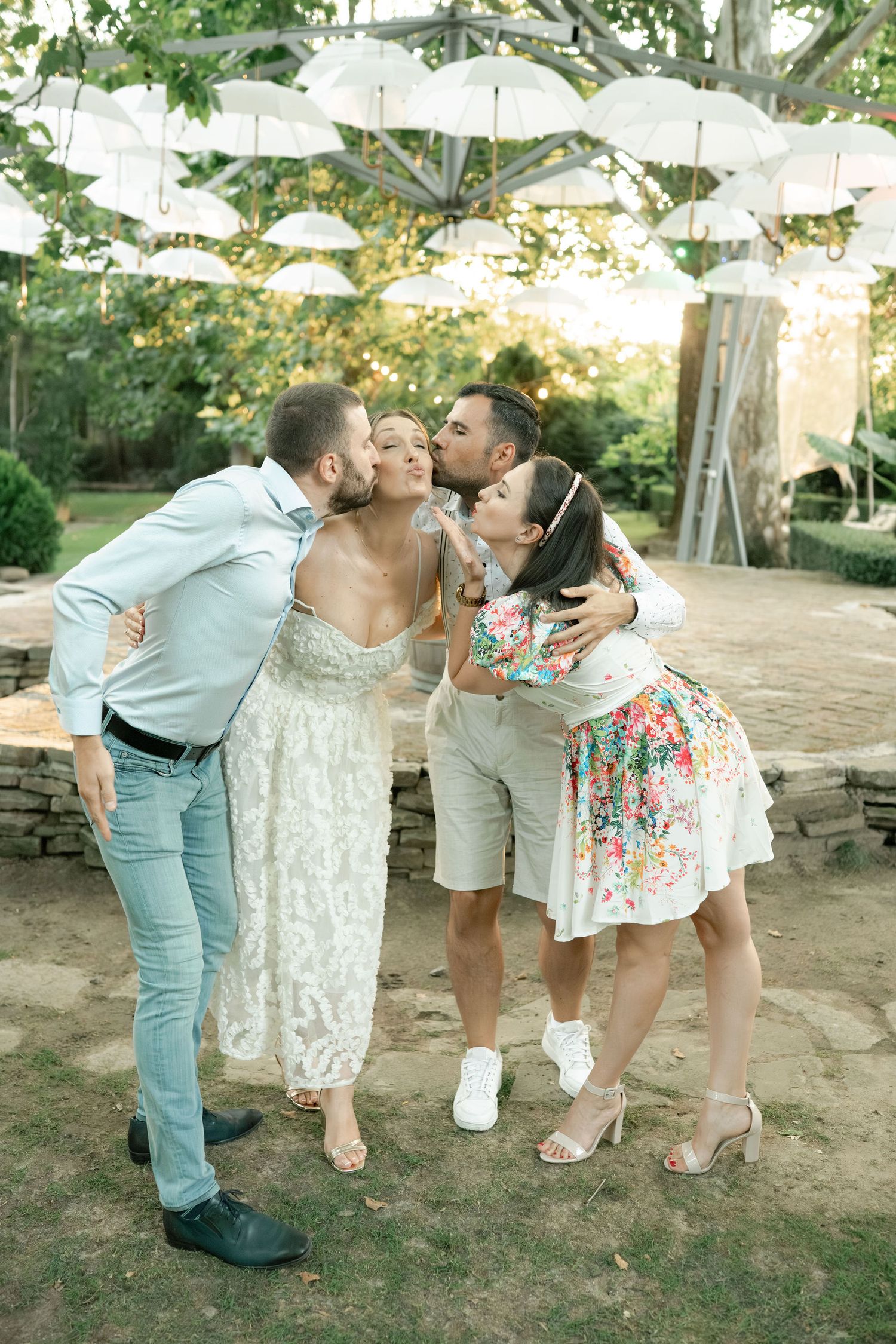 Group of friends sharing playful kisses outdoors in a garden setting during a casual summer gathering.