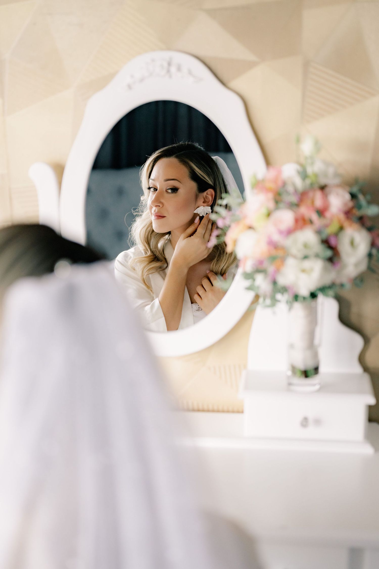 A series of elegant bridal preparation photos reflected in white-framed vanity mirrors with soft floral decorations.