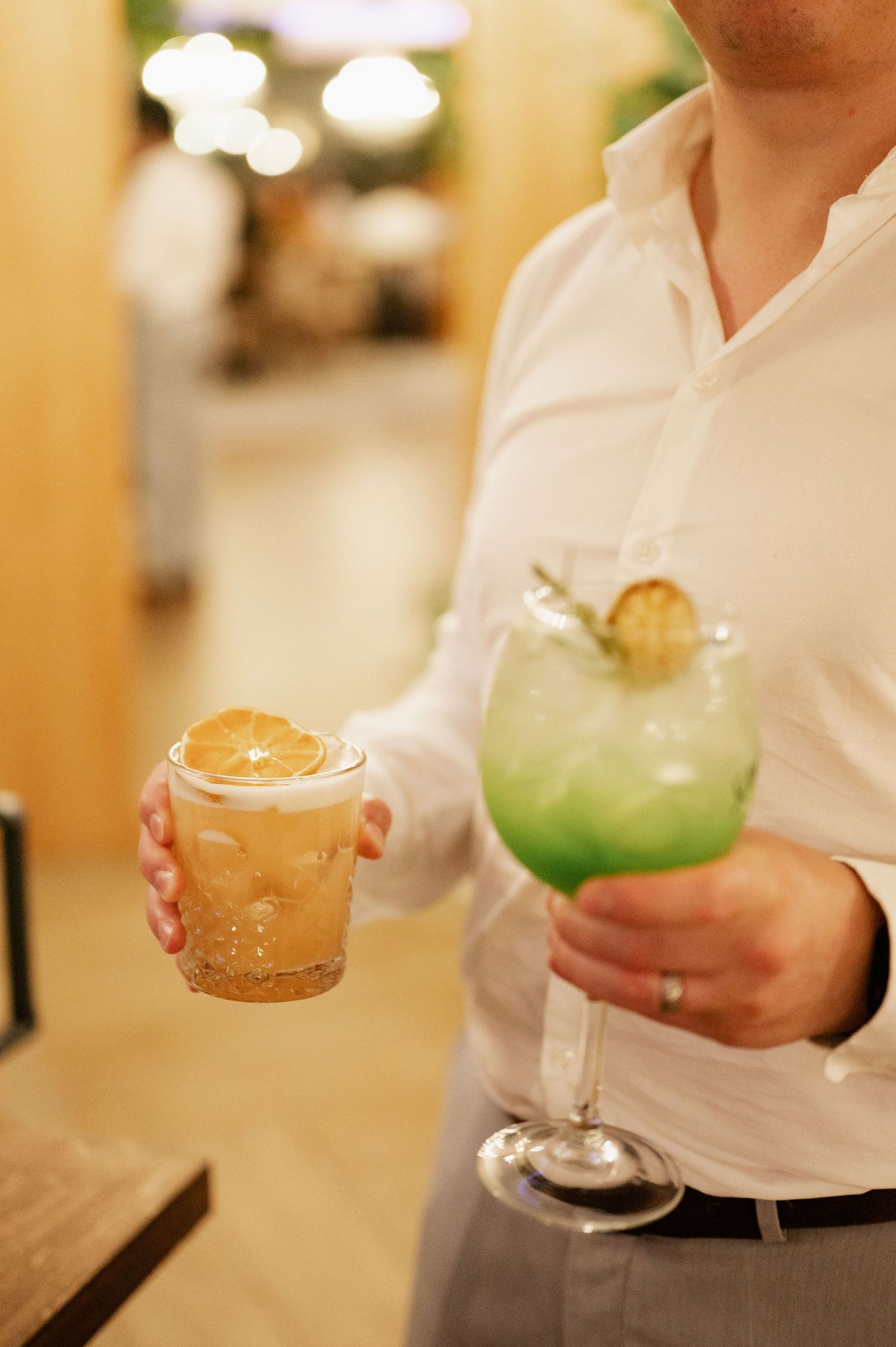 A row of elegant cocktail glasses being served on a bar with different colored drinks and garnishes.