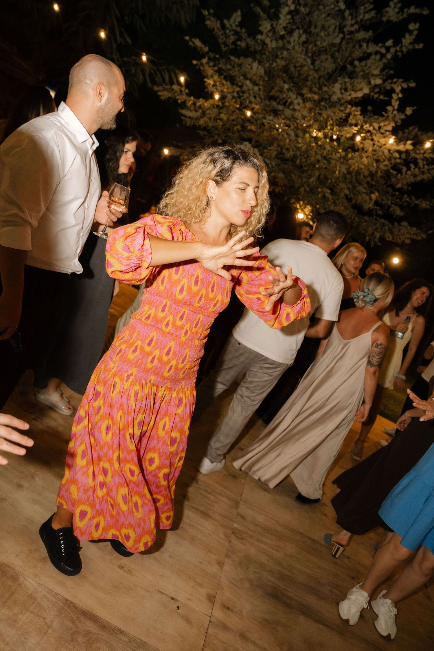Dancers move energetically on a wooden dance floor under string lights at an outdoor evening celebration.