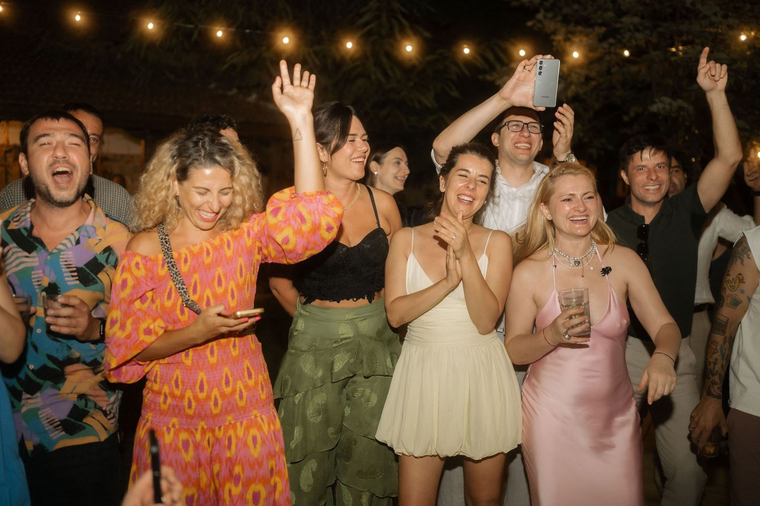 A group of people dancing and celebrating at a lively outdoor nighttime party or reception.