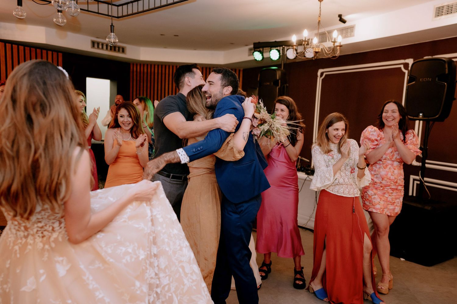 Wedding guests dance together during reception celebration at an indoor venue with warm lighting.