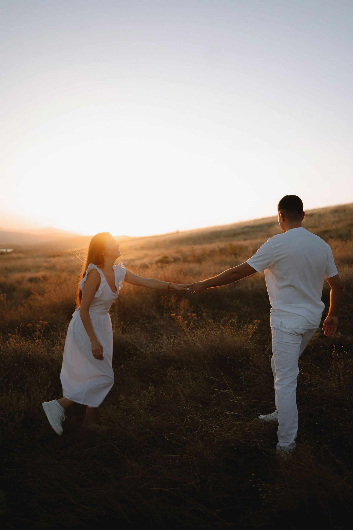 Silhouette of person in white clothing walking across a grassy hill at sunset with golden light in background.