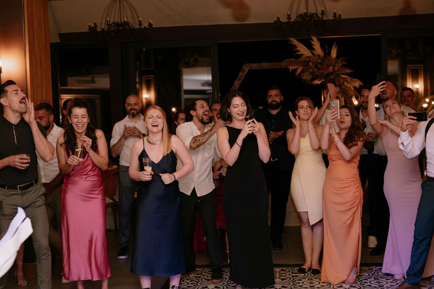 A group of wedding guests dancing and celebrating together on a dance floor at an evening reception.