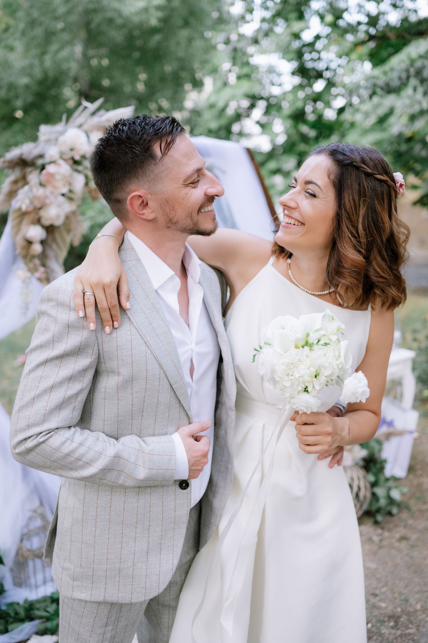A joyful couple shares intimate moments in their wedding attire against a natural outdoor backdrop.