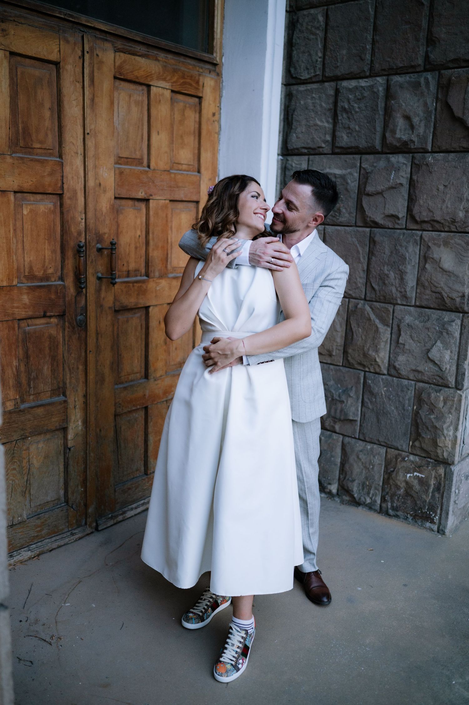 A romantic couple in white outfits share tender moments in a series of three photos against a stone wall and wooden doors.