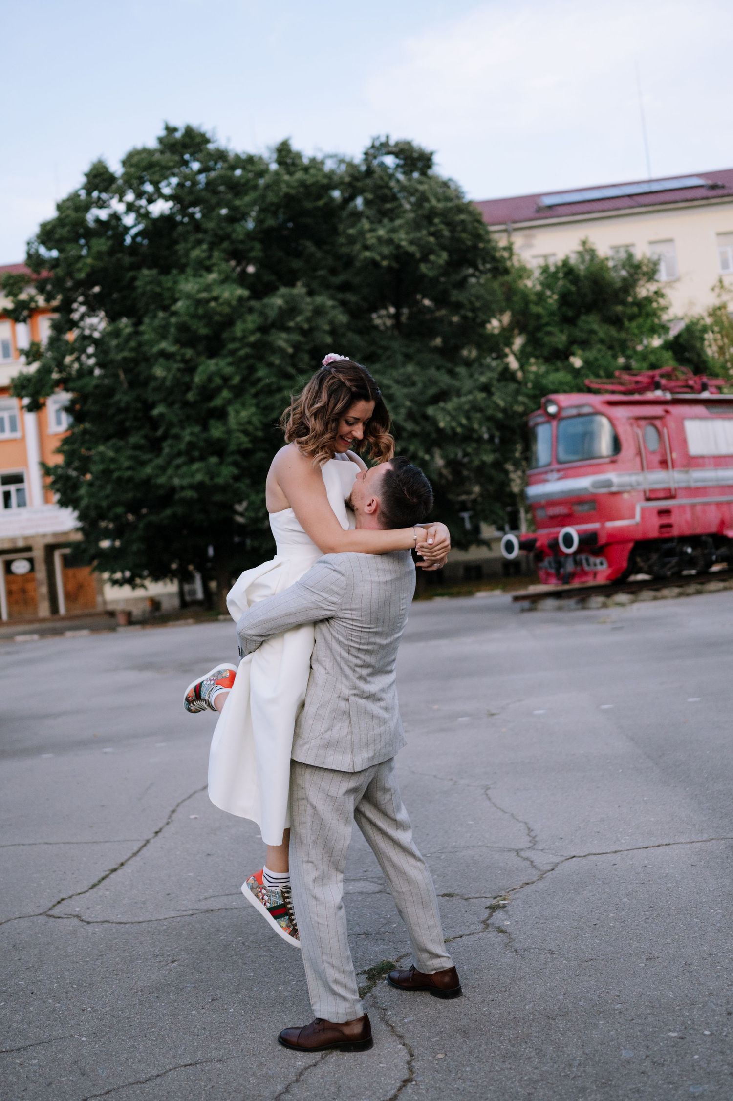 A couple in casual attire dances and embraces in an empty parking lot on a summer day.