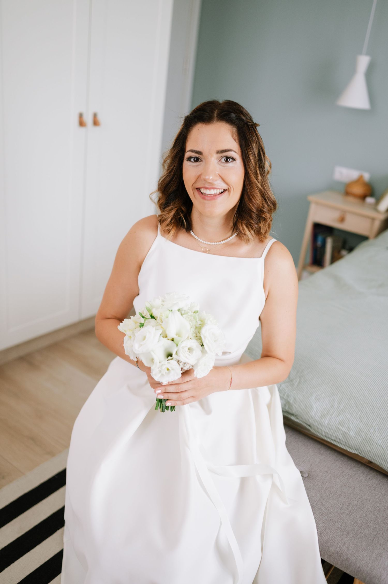 A bride in a white sleeveless dress sits gracefully holding a delicate bouquet of white flowers.
