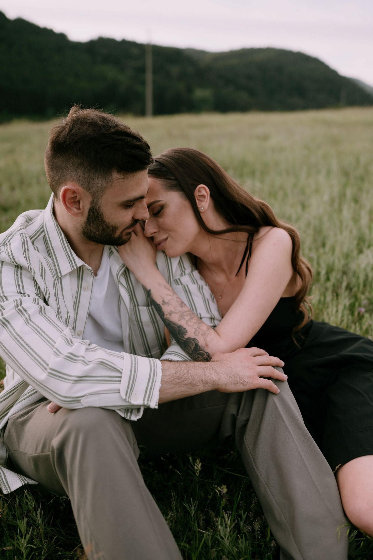 A couple shares an intimate moment together while sitting in a grassy field on a summer afternoon.