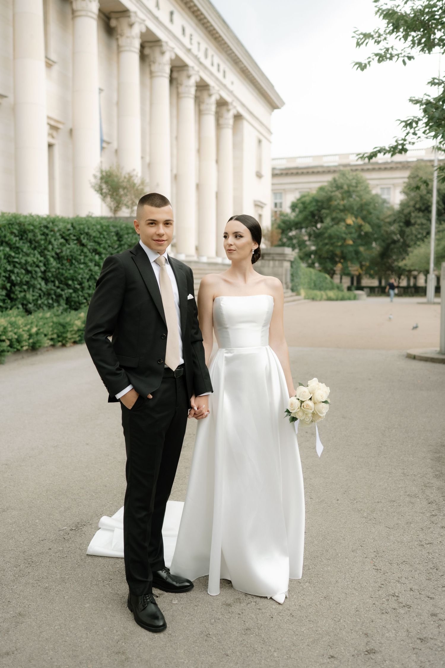 A wedding couple poses elegantly in front of a neoclassical building with white columns.