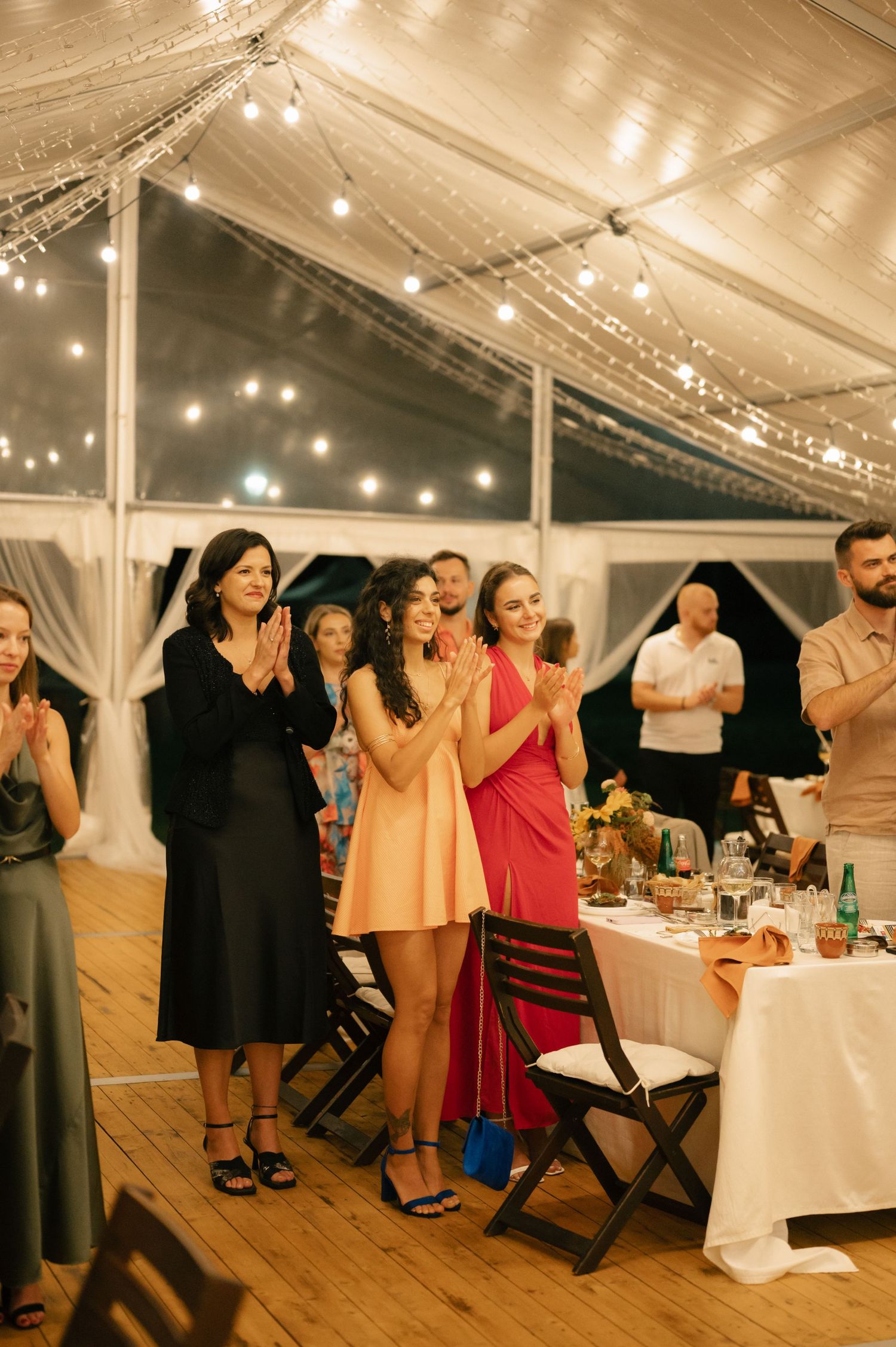 Wedding guests dance and celebrate under a white tent with string lights and elegant table settings.